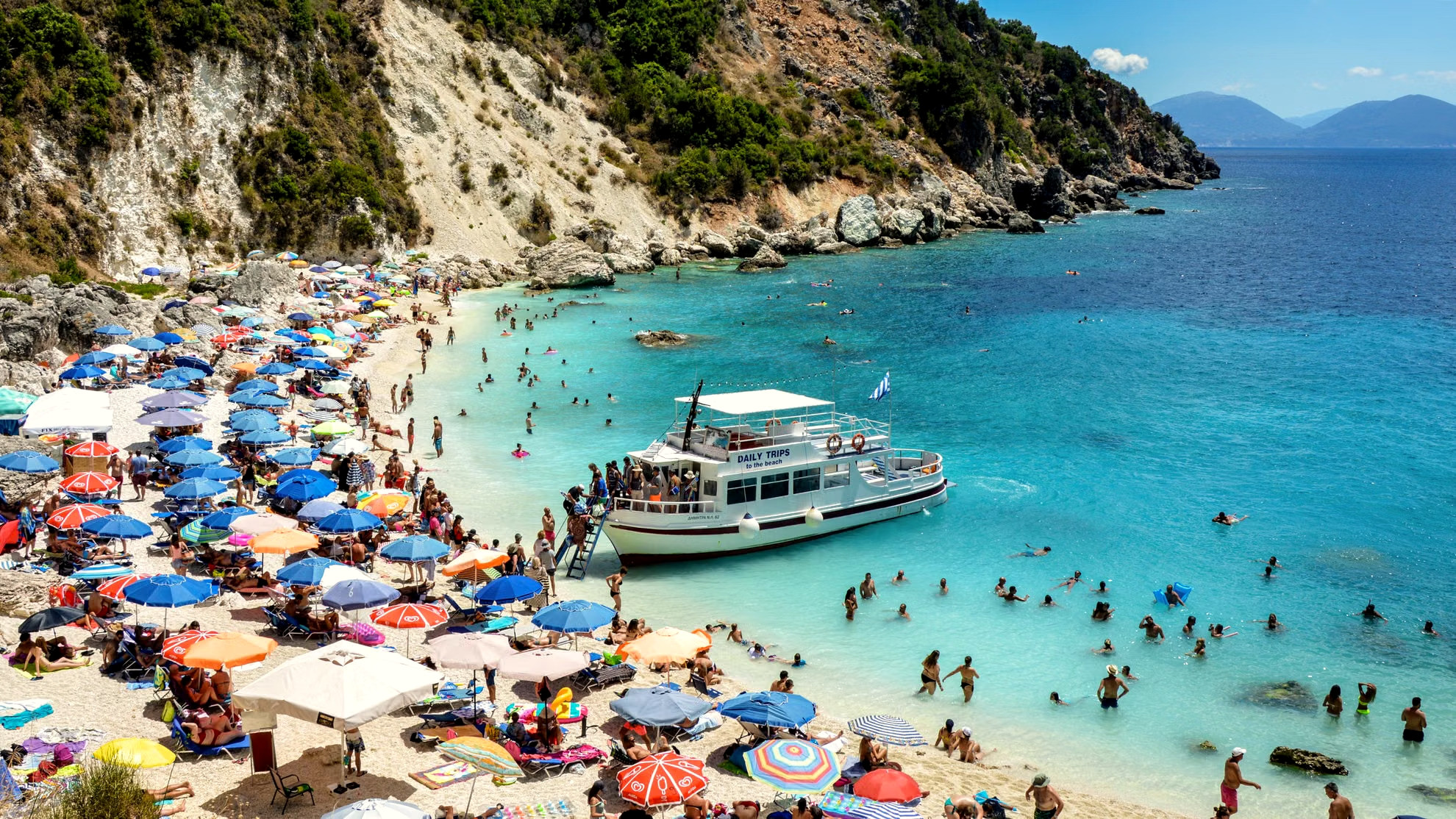 Busy beach and ferry in high summer - Greece