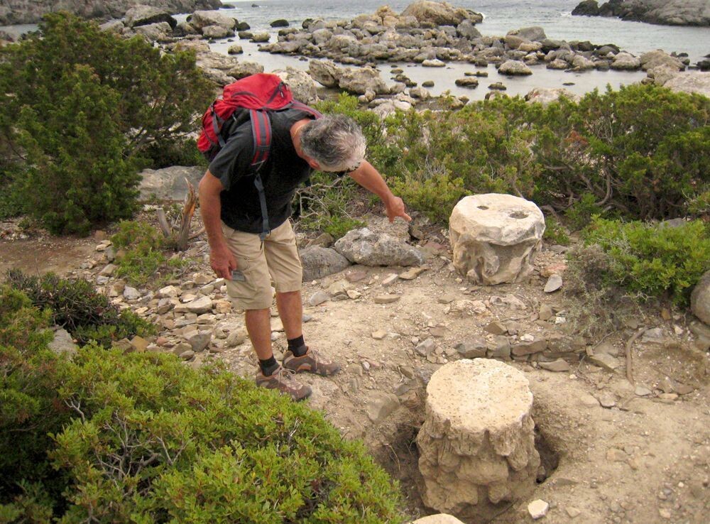 Randonneur examinant des chapiteaux antiques sur la côte rocheuse - Grèce