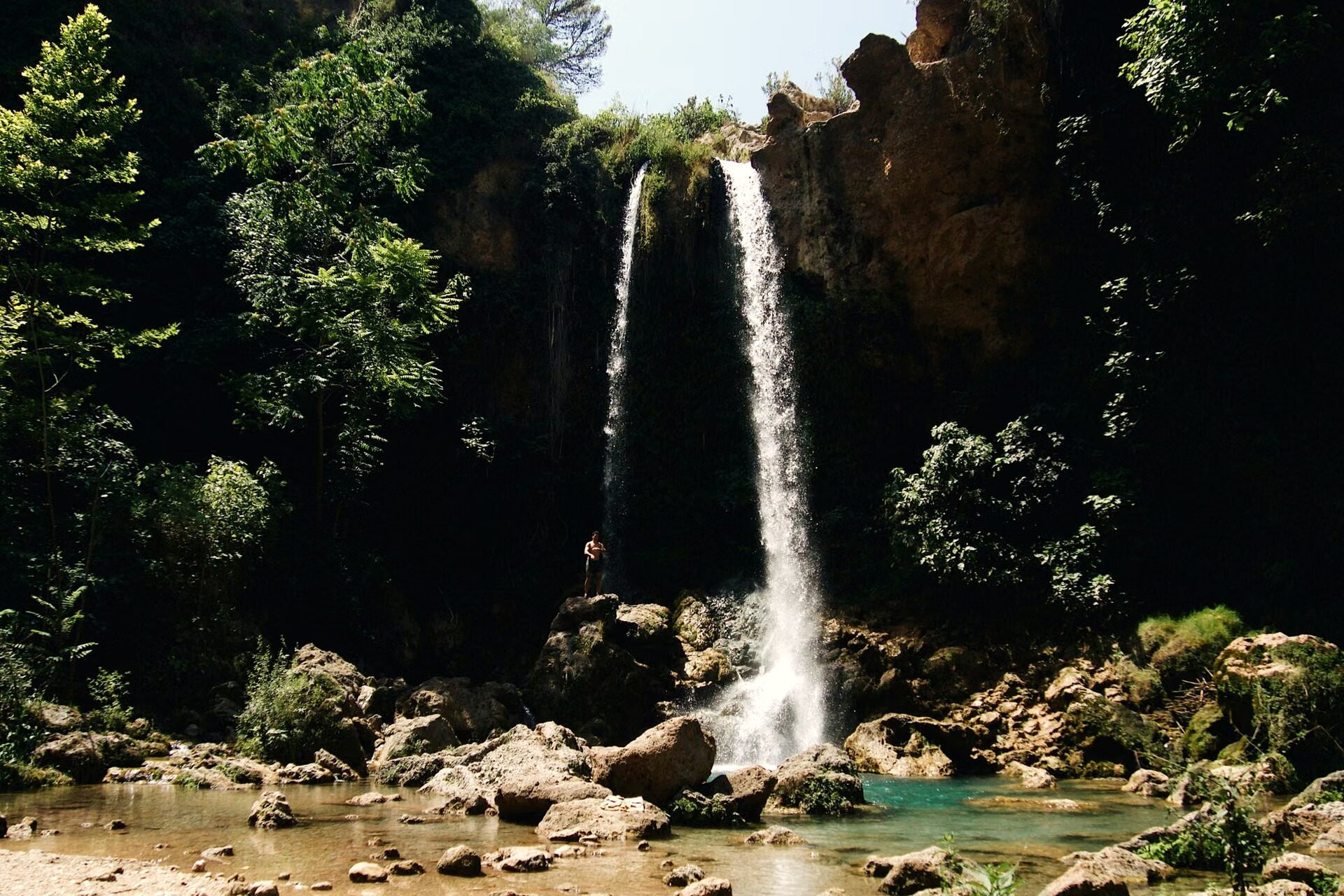 Waterfall dropping into a pool of clear water at the bottom of a wooded gorge - Crete, Greece