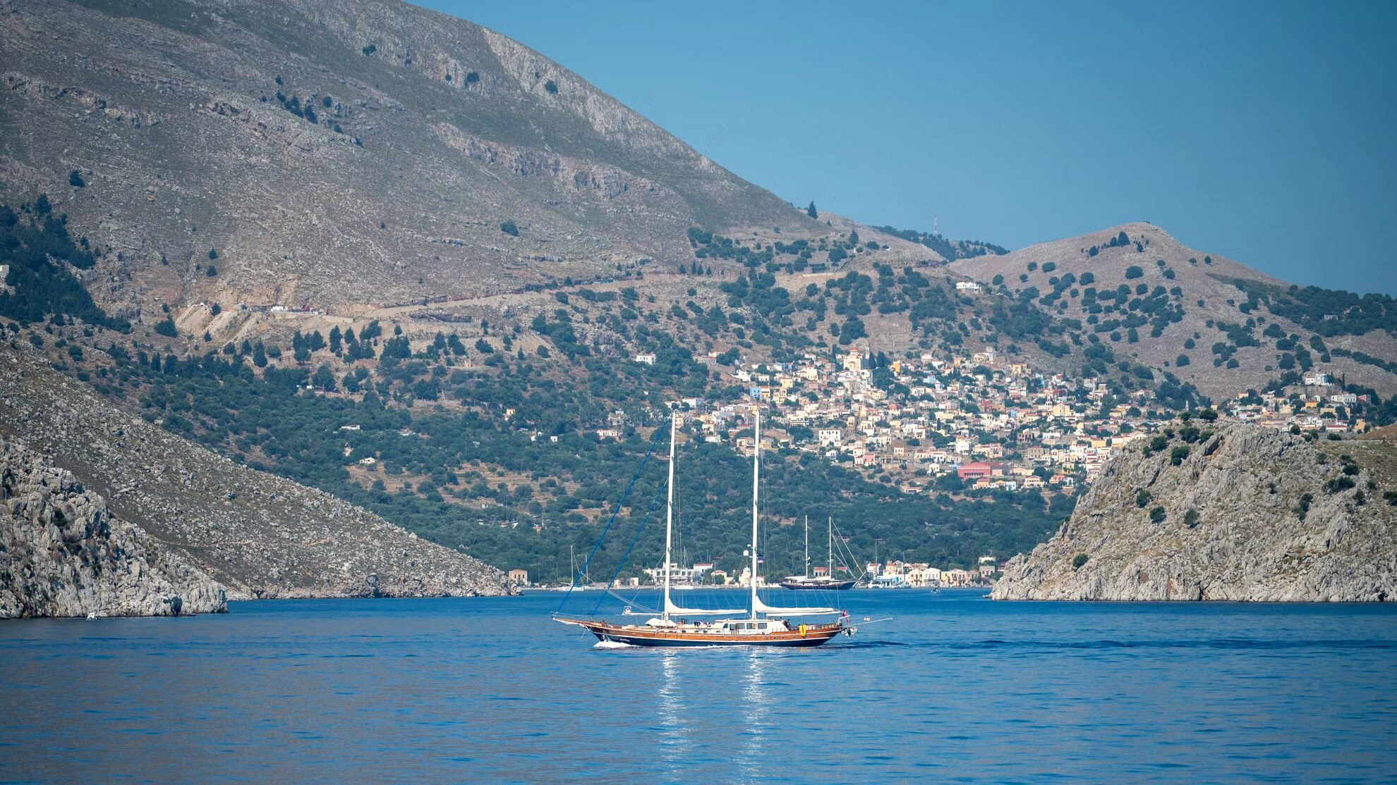 Sailboat anchored in a bay at the foot of the cliffs - Symi - Greece